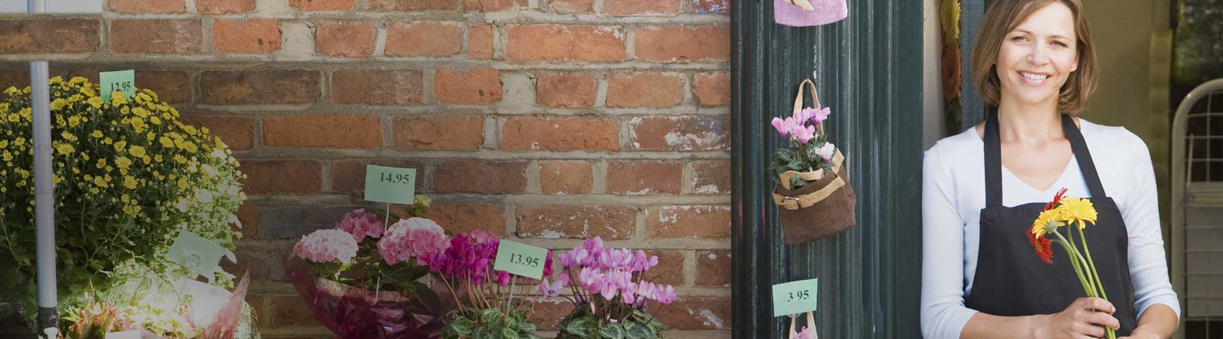 Female florist smiling with flowers in front of business